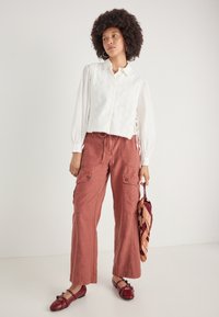 Biely crop top s očkami a krátkymi rukávmi, v kombinácii s rustovými širokými cargo nohavicami s vreckami a červenými balerínkami. Pridaný doplnok.