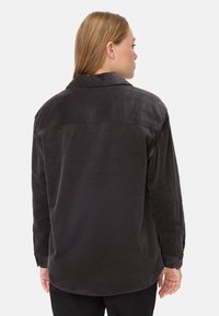 Dunkelgraue Cord-Hemdjacke mit Kragen, langen Ärmeln und einer gerippten Textur. Verfügt über einen verlängerten Saum und eine glatte Oberfläche.