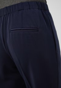 Námořnické modré kalhoty s hladkou texturou, vybavené elastickým pasem a úzkou zadní kapsou s minimálním designovým detailem.