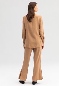 Blusa color tortora e pantaloni palazzo abbinati, realizzati in tessuto leggero, con spacchi laterali all'orlo e maniche lunghe con polsini bottonati.