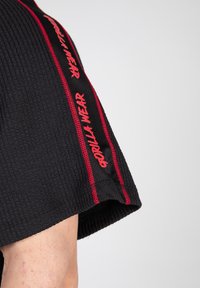 Zwarte textuurshirt met korte mouwen. Rode branding "GORILLA WEAR" langs de zijkant. De stiksels verbeteren het algehele ontwerp.