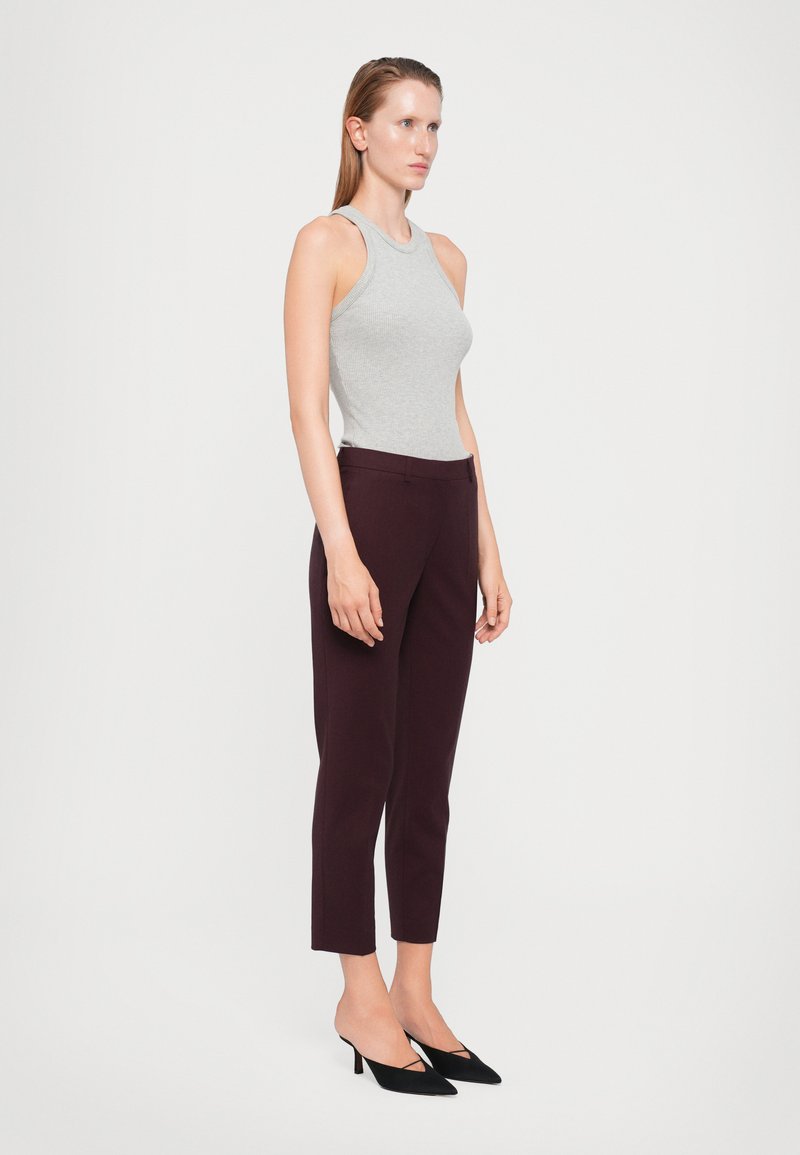 Grijze geribbelde tanktop, bordeauxrode nauwsluitende broek, zwarte puntige hakken. Schone lijnen en op maat gemaakte silhoutte. Glad textuur overal.