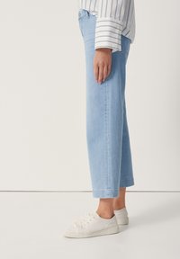 Světle modré džínové kalhoty s přímým střihem, zkrácené délky a jemným vyblednutím, doplněné bílými plátěnými teniskami.