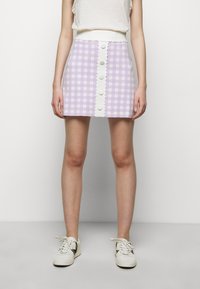 Lila rutigt mini kjol med vit knappfront och scallopmidja, tillverkad av ett texturerat tyg. Bärs med vita sneakers.