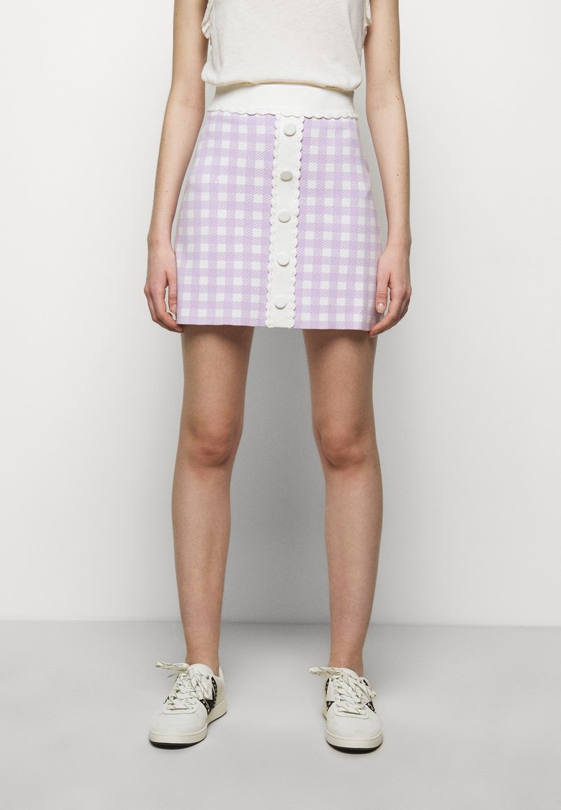 Lila rutigt mini kjol med vit knappfront och scallopmidja, tillverkad av ett texturerat tyg. Bärs med vita sneakers.