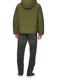 Pufferjack in olijfgroen met een capuchon en een geborduurd textuur, gecombineerd met donkergrijze spijkerbroek en zwarte sneakers met witte zolen.