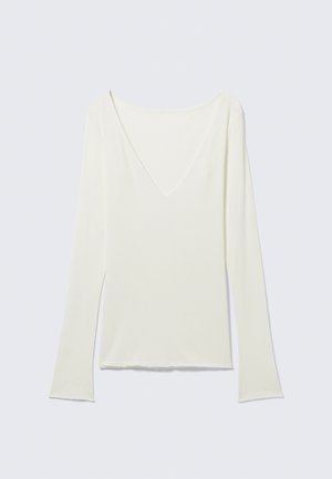 Λευκό μακρυμάνικο εφαρμοστό τοπ με βαθύ V ντεκολτέ και ελαφρώς φαρδιές μανσέτες, παρουσιάζεται σε απλό ανοιχτό γκρι φόντο.