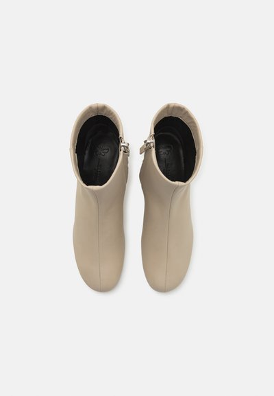 Botine din piele bej, cu o textură netedă, dotate cu închidere cu fermoar și vârfuri rotunjite moi. Interiorul este negru, cu un branding subtil.