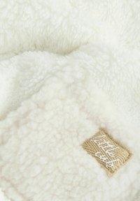 Weißer Fleece-Decke mit einer weichen, plüschigen Textur. Ein beiges Etikett mit weißer Stickerei ist in eine Ecke genäht.