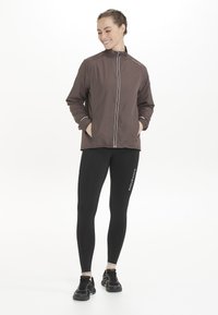 Brun jacka med hög krage och vit dragkedjedetalj, tillsammans med svarta leggings med texten "ENDURANCE". Båda plagg är åtsittande och lätta.