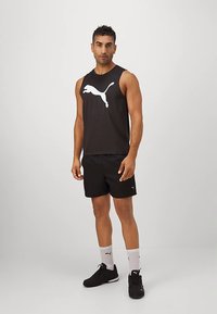 Must mustaga tank top, millel valge Puma logo, kombineeritud mustade lühikeste pükstega. Mudel kannab musti tossusid ja valgeid sokke.
