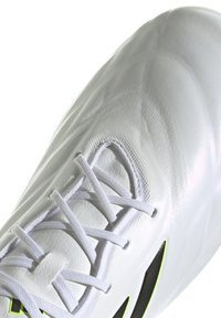 Scarpa da calcio bianca con materiale sintetico testurizzato, caratterizzata da un design aerodinamico, un sistema di lacci prominente e accenti in nero e verde neon.