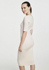 Klejąca sukienka wykonana z prążkowanego materiału w jasnym beżu z krótkimi rękawami i zapięciem z tyłu. Sukienka o długości do kolan podkreśla kontur ciała.