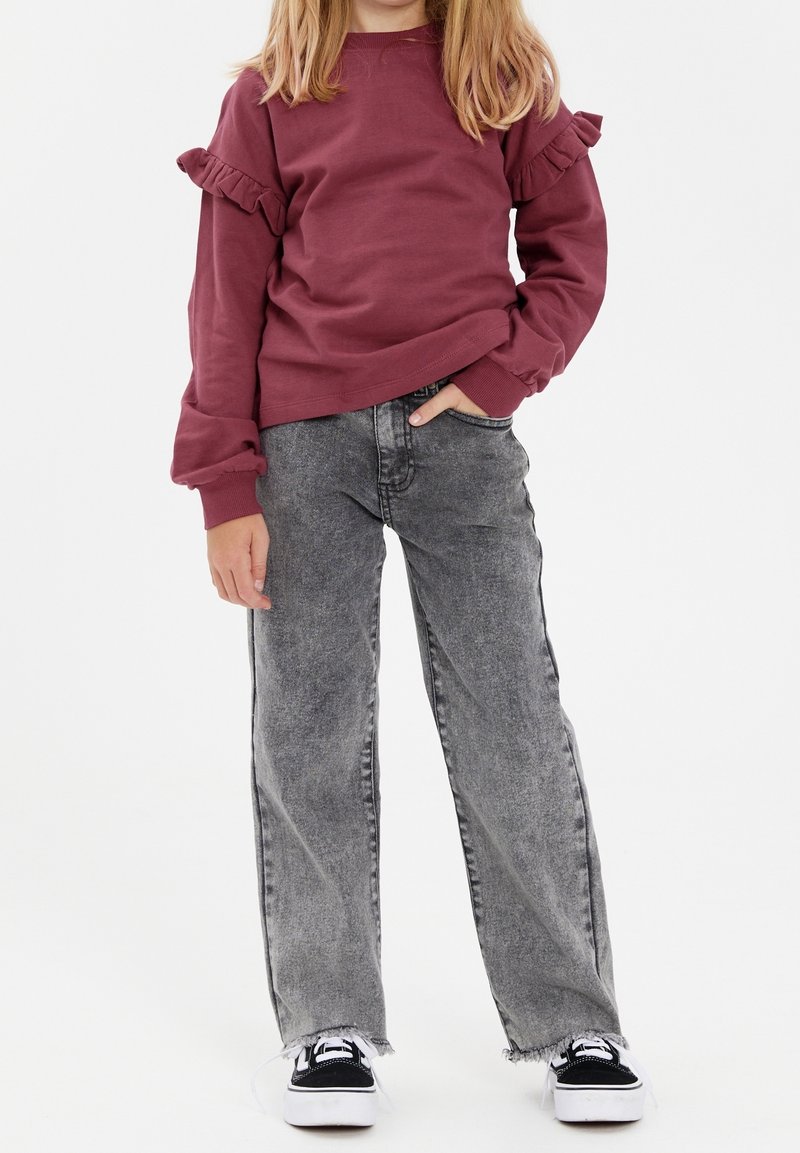 Bordeauxfarbiges Sweatshirt mit Rüschensleeves, kombiniert mit ausgewaschenen, schwarzen Schlagjeans und schwarzen Sneakers. Das Outfit hat einen lässigen Look.