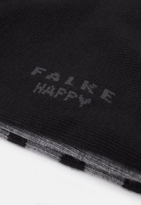 Sort strikket tørklæde med små grå prikker, der har teksten "FAKE HAPPY" i en kontrasterende farve langs kanten. Teksten har en subtil tekstur.