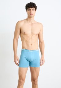 Hellblaue Boxer-Brief mit einer weichen Textur, ausgestattet mit einem grauen elastischen Bund, der mit "BOSS" beschriftet ist. Das Design ist passgenau und glatt.