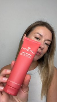 GECORRIGEERD: Roze tube van Origins Youthtopia Apple Butter Cleansing Balm met witte tekst en een klapdeksel, vastgehouden door een persoon met licht haar.