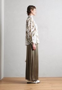 Blusa a maniche lunghe con motivo floreale in tessuto leggero; gonna maxi verde oliva larga; scarpe flat bianche; vista laterale su uno sfondo neutro.