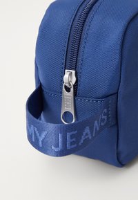 Borsa di tessuto blu con superficie texture, zip argentata e manico intrecciato che presenta il testo "I MIEI JEANS" in un blu più chiaro.