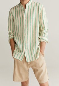 Leinenhemd mit vertikalen grünen und cremefarbenen Streifen, Stehkragen, Knopfleiste und langen Ärmeln, kombiniert mit beigefarbenen Shorts.