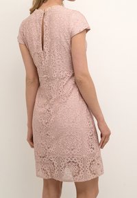 Robe en dentelle de couleur rose clair avec des manches courtes, présentant des motifs floraux complexes, une ouverture en forme de clé dans le dos et une silhouette ajustée.