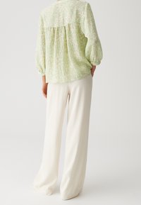 Blusa verde chiaro a maniche lunghe con un motivo testurizzato, vita stretta e fit rilassato sul retro, abbinata a pantaloni bianchi a gamba larga.