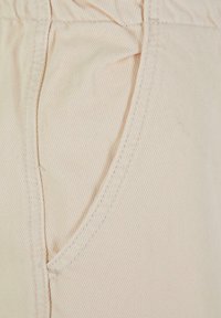 Beige stoff med skrå ribbet tekstur, med en sydd sidelomme. Mykt materiale og elastisk midje.