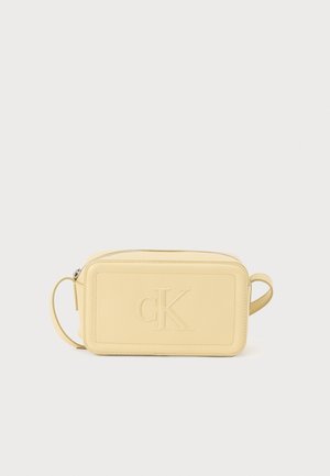 Sac rectangulaire en cuir jaune avec logo 'cK' embossé, fermeture éclair et poignée latérale. Texture lisse avec bords cousus.