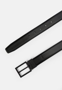 Μαύρη δερμάτινη ζώνη με λεία υφή, που διαθέτει ορθογώνια μεταλλική αγκράφα και πέντε τρύπες ρύθμισης κατά μήκος του λουριού.