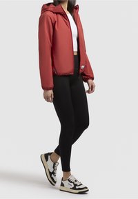 Red lightweight jacket with a hood, zip front, and elastic cuffs; paired with black leggings and black-and-white sneakers.