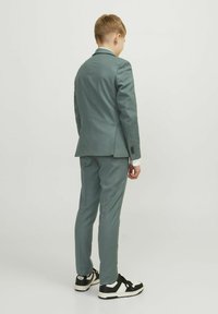 Completo per bambini in tessuto verde chiaro, giacca monopetto con rever a lancia, pantaloni slim-fit e camicia bianca. Accenti di sneaker in bianco e nero.