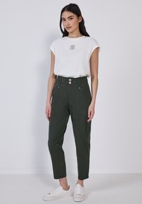 T-shirt bianco a maniche corte con grafica "OWN THE DAY", abbinato a pantaloni hi-waist verde scuro e sneaker bianche. Design minimalista.