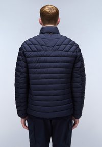 Námořnická pufovaná bunda s prošívaným designem, vysokým límcem a žebrovaným lemem. Tkanina vypadá hladce s lehkou, izolovanou strukturou.