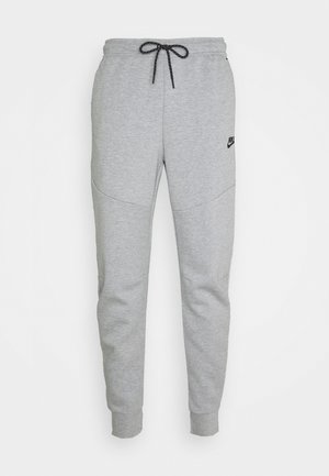 Pantaloni della tuta Nike grigio chiaro con coulisse nera, polsini elasticizzati e piccolo logo Nike nero sulla parte superiore della coscia sinistra.