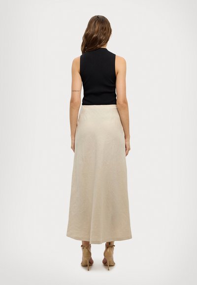 Top senza maniche nero a costine abbinato a una gonna beige alla caviglia realizzata in un tessuto leggero, con una sottile trama e una silhouette fluida.