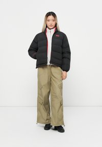 Cazadora corta negra acolchada con detalles rojos, combinada con pantalones cargo holgados en color caqui. La cazadora tiene un cuello alto y una textura acolchada.
