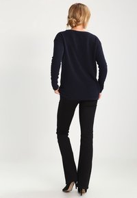 Maglione blu navy a maniche lunghe con tessuto testurizzato, vestibilità rilassata e orlo asimmetrico, abbinato a pantaloni neri attillati e scarpe con tacchi alti nere.