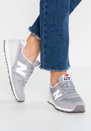 Harmaat New Balance 996 -lenkkarit, joissa on mokka- ja verkko-yläosa, valkoinen logo ja harmaa pohja, yhdistettyinä farkkuihin, joissa on revitty helma.