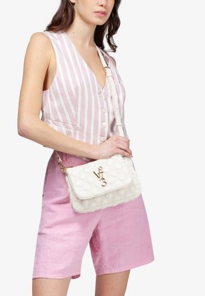 Donna che indossa una canottiera a righe rosa e bianche senza maniche e pantaloncini rosa, che tiene una borsa a tracolla bianca trapuntata con emblema dorato.