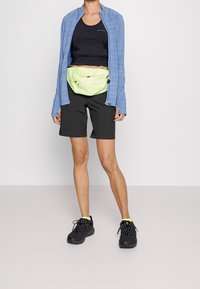 Vaaleansininen vetoketjullinen takki, musta lyhyt toppi, mustat shortsit ja kirkkaan vihreä vyölaukku. Mustat kengät keltaisilla yksityiskohdilla. Yksinkertainen muotoilu, rento istuvuus.