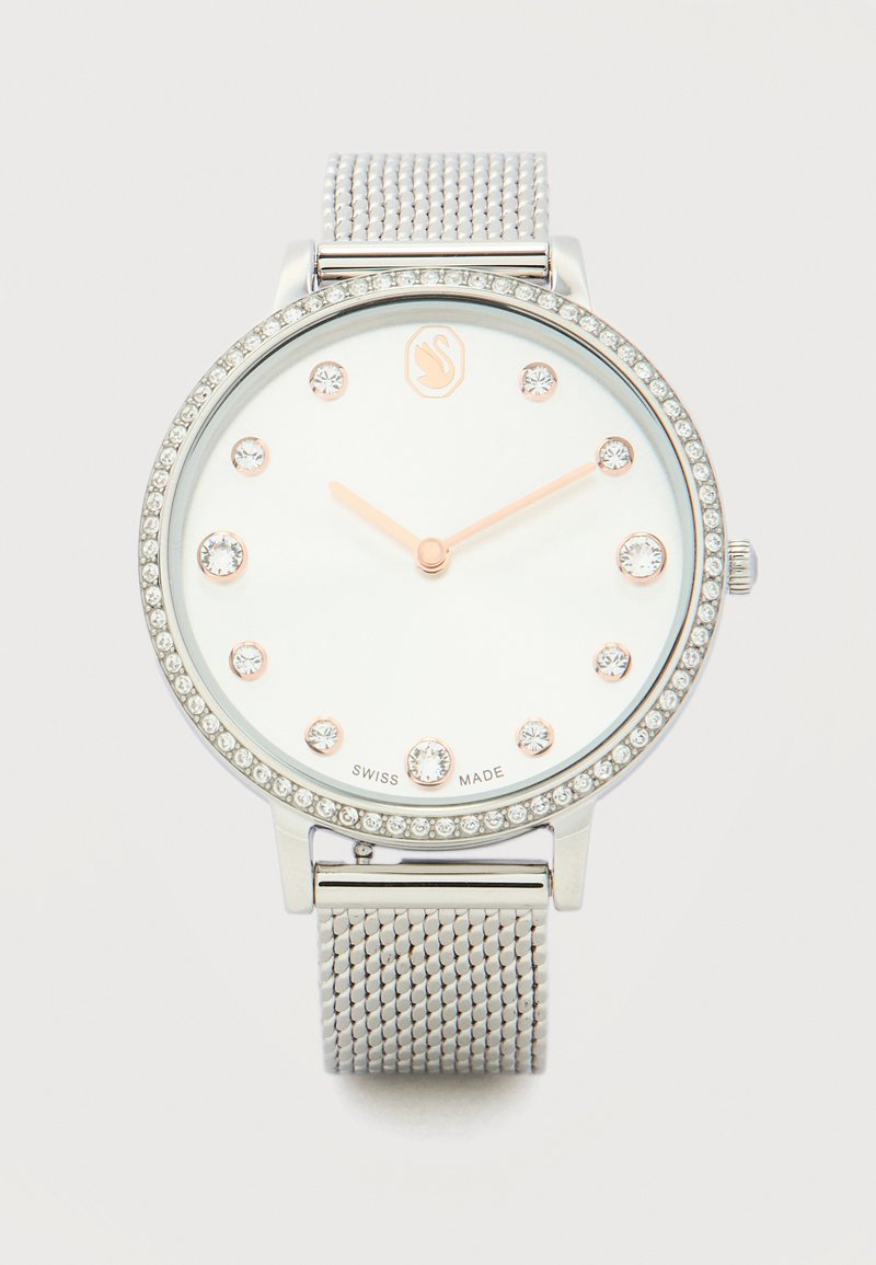 Στρογγυλό ασημένιο ρολόι με στεφάνη διακοσμημένη με κρύσταλλα, μπάντα από πλέγμα, λευκό καντράν, δείκτες ώρας από κρύσταλλα και χρυσούς δείκτες που δείχνουν 10:10.