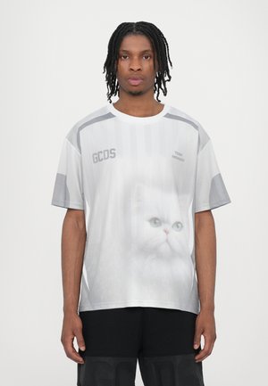 T-shirt bianco a maniche corte con grafica di un gatto, caratterizzato da righe verticali e accenti grigi. Il materiale sembra leggero e traspirante.