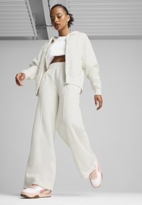 Sudadera con capucha de felpa de color claro y pantalones anchos a juego. Zapatillas blancas con detalles en rosa. Diseño simple y corte relajado.