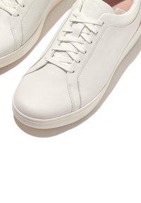 Weiße Leder-Sneaker mit glatter Oberfläche, runder Zehenform, flachen Schnürsenkeln und dezenter Markierung auf der Zunge. Helles pinkes Innenfutter.