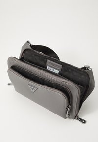 Borsa a tracolla sintetica grigia con più compartimenti con cerniera. L'interno presenta una fodera nera con un motivo a logo ripetuto e dettagli in metallo argentato.
