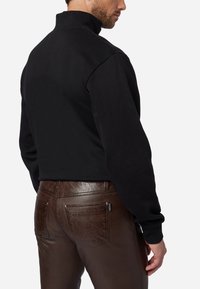 Zwarte high-neck sweatshirt met lange mouwen, gecombineerd met bruine leren broek met achterzakken en een gladde textuur.