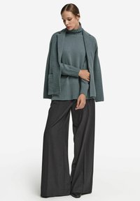 Mjuk turkos polotröja med ribbad nederkant, kombinerad med löst sittande, högmidjade byxor i kolagrå. Ensemblen har en avslappnad silhuett.