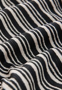 Tessuto nero e crema con strisce ondulate e superficie testurizzata, che mette in mostra un design decorato in colori alternati e larghezze variabili.