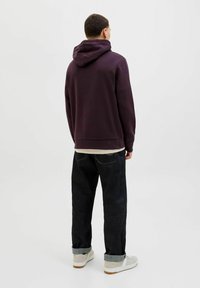 Maronfarvet hoodie med en stor hætte, afslappet pasform, kombineret med mørke denimjeans. Sneakers med en lys overdel og hvid sål fuldender outfittet.