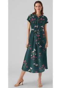 Robe midi verte à imprimé floral, à manches courtes, avec une taille ceinturée et un bas fluide. Présente des fleurs roses et blanches sur un fond sombre.